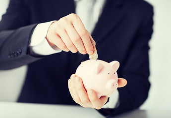 Image showing man putting coin into small piggy bank