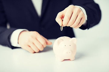 Image showing man putting coin into small piggy bank