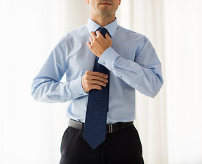 Image showing close up of man in shirt adjusting tie on neck