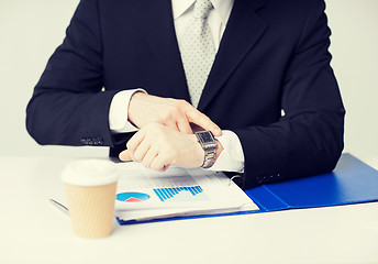 Image showing businessman with graphs pointing at watch