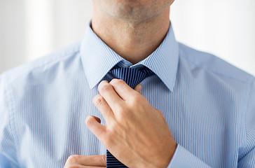 Image showing close up of man in shirt adjusting tie on neck