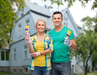 Image showing smiling couple with paint brushes over house