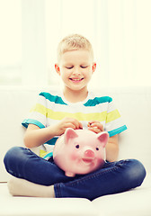 Image showing smiling little boy with piggy bank at home