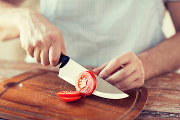 Image showing male hand cutting tomato on board with knife