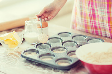 Image showing close up of hand filling muffins molds with dough