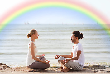 Image showing happy couple meditating in lotus pose on beach