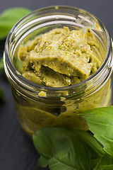 Image showing Glass jar with basil pesto on a black plate