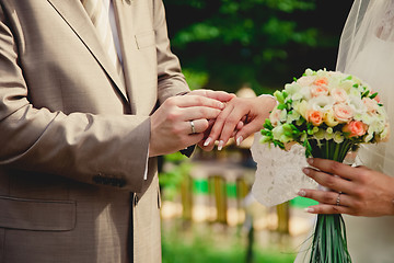 Image showing mans hand putting a wedding ring on the brides finger