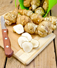 Image showing Jerusalem artichokes cut with knife and green bucket on board