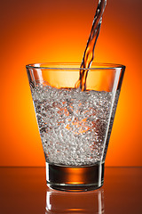 Image showing pour water into a glass on orange background