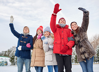 Image showing happy friends waving hands on ice rink outdoors