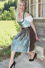 Image showing Smiling woman in dirndl sitting on an old bench