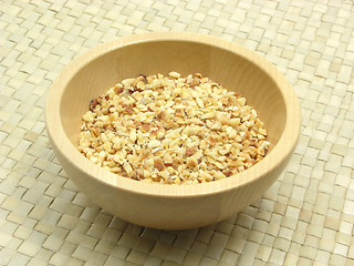 Image showing Wooden bowl with roasted chopped hazelnuts on rattan underlay