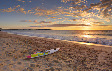 Image showing Beach sunrise and paddleboard on shoreline