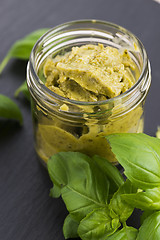 Image showing Glass jar with basil pesto on a black plate