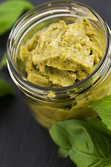 Image showing Glass jar with basil pesto on a black plate