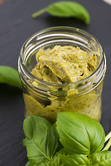 Image showing Glass jar with basil pesto on a black plate