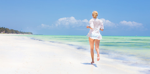 Image showing Woman running on the beach in white shirt. 