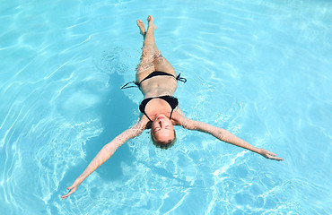 Image showing Beautiful Caucasian lady floating in swimming pool.