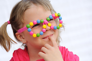 Image showing Portrait of cute little girl wearing funny glasses, decorated with colorful sweets, smarties, candies