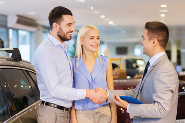 Image showing happy couple with car dealer in auto show or salon