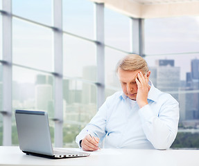 Image showing senior man with laptop and pen writing at office