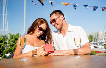 Image showing smiling couple with champagne and gift at cafe