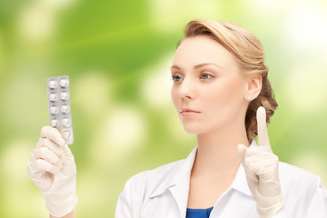 Image showing young female doctor with pills pointing finger up