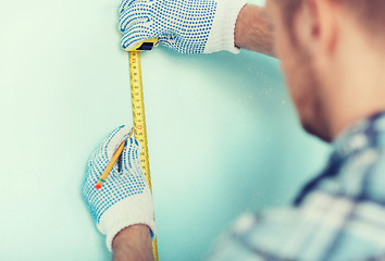 Image showing closeup of male in gloves measuring wall with tape