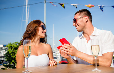 Image showing smiling couple with champagne and gift at cafe