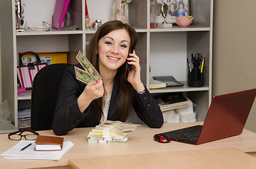 Image showing The girl in the office with a bundle of banknotes talking on phone