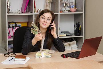 Image showing girl a office talking on phone and looking at paper money in hand