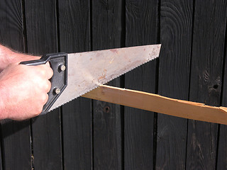 Image showing Cutout with hand and hand saw in front of a wooden wall