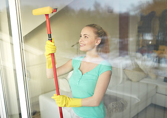 Image showing happy woman in gloves cleaning window with sponge