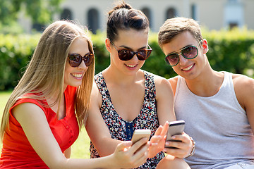 Image showing smiling friends with smartphones sitting in park