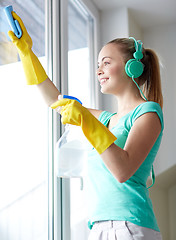 Image showing happy woman with headphones cleaning window