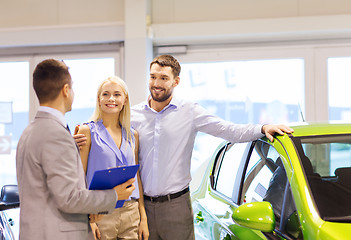 Image showing happy couple with car dealer in auto show or salon