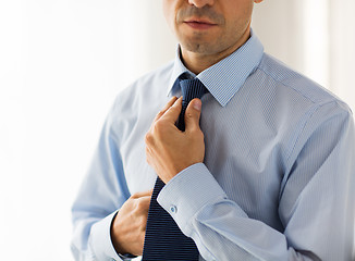 Image showing close up of man in shirt adjusting tie on neck