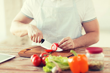 Image showing male hand cutting tomato on board with knife