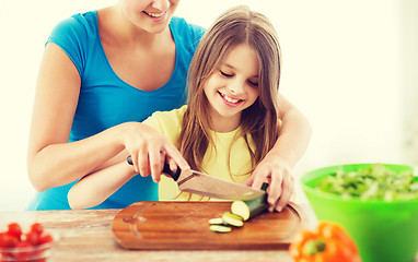 Image showing smiling little girl with mother chopping cucumber