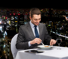 Image showing smiling man with tablet pc eating main course