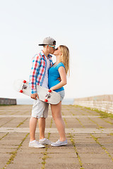 Image showing smiling couple with skateboard kissing outdoors