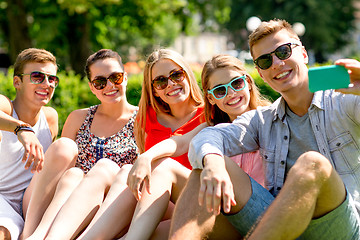 Image showing smiling friends with smartphone sitting on grass