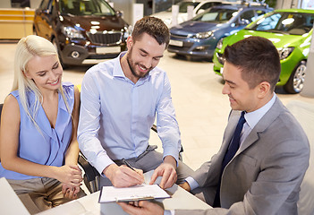 Image showing happy couple with car dealer in auto show or salon