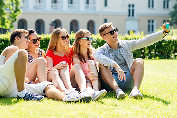 Image showing smiling friends with smartphone sitting on grass