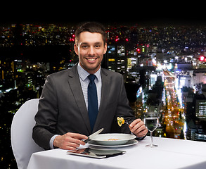 Image showing smiling man with tablet pc eating main course