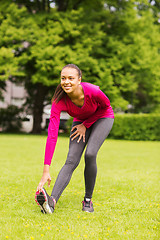 Image showing smiling black woman stretching leg outdoors