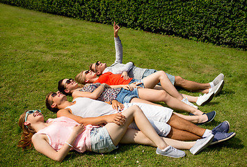 Image showing group of smiling friends lying on grass outdoors