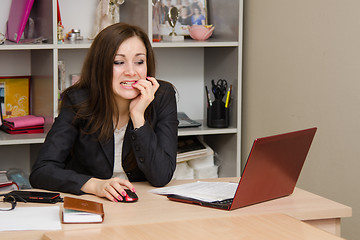 Image showing Nervous girl in office bites his nails, working on computer