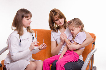 Image showing Pediatrician holding a syringe for sick child sitting on hands of mother